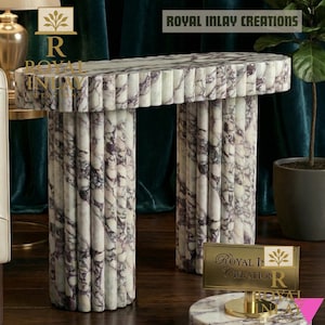 Puede incluir: Una consola de mármol con un diseño acanalado. La mesa tiene una parte superior rectangular y dos patas cilíndricas. El mármol es blanco con vetas moradas oscuras. El texto "ROYAL INLAY CREATIONS" es visible.