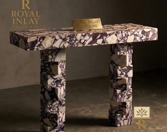 May include: A rectangular marble table with a purple and white pattern. The table has two stacked pillar legs. A small gold sign on the table reads "ROYAL INLAY CREATIONS". The table is a unique piece of furniture.