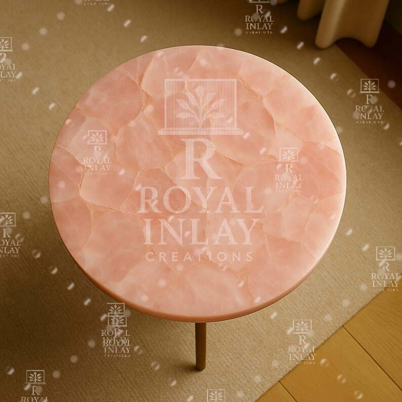 May include: A round pink table with a natural stone top. The table is made of rose quartz and has a unique, textured surface. The table is supported by a single, gold-colored leg.