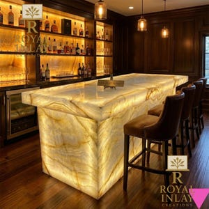 May include: A backlit bar with a marble-effect surface, set against dark wood paneling and shelving stocked with bottles. Brown leather bar stools are in front of the bar. The logo "Royal Inlay Creations" is visible. Overhead, pendant lights illuminate the scene.