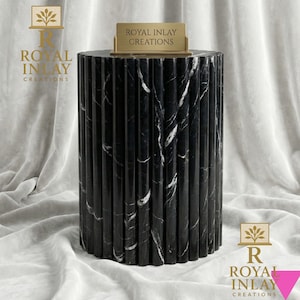 Può includere: Un tavolino in marmo bianco e nero con un design scanalato. Il tavolo ha una forma cilindrica e un cartello dorato sulla parte superiore con la scritta "ROYAL INLAY CREATIONS". Il tavolo è alto circa 61 cm.