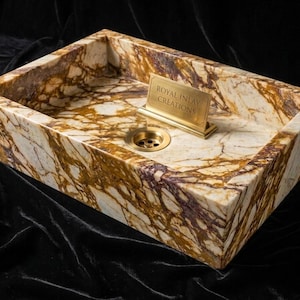 May include: A rectangular stone sink featuring a cream, brown, and deep purple marbled pattern. The basin includes a brass-colored drain and a small, upright brass-colored plaque engraved with the text ROYAL INLAY CREATIONS.