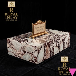 May include: A rectangular marble block with a white and burgundy pattern. A gold-framed sign with the text "ROYAL INLAY CREATIONS" sits on top. The Royal Inlay Creations logo is in the top left and bottom right corners.