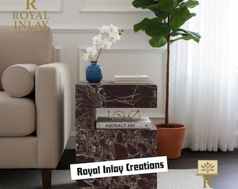 May include: A modern side table with a dark brown marble-like pattern. The table has a unique design with open shelving. A blue vase with white flowers, a book, and eyeglasses are on the table. The text "Royal Inlay Creations" is visible.