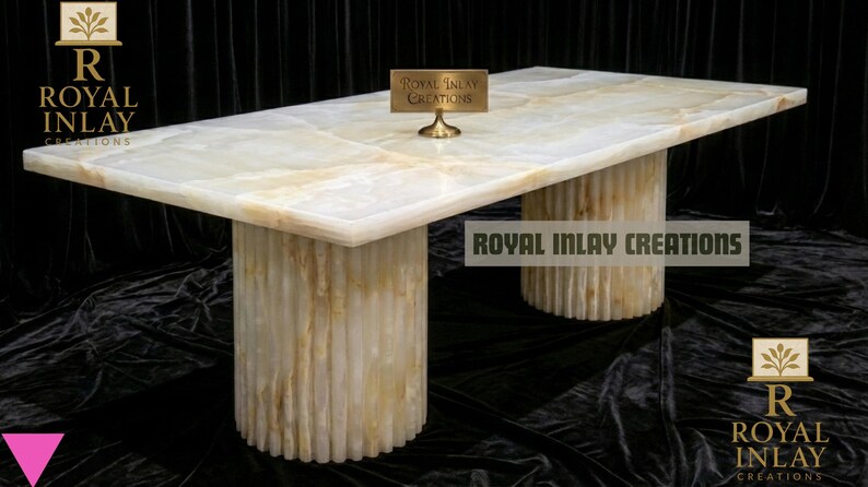 May include: A rectangular onyx table with a light cream and gold color scheme. The table has a smooth, polished surface and is supported by two cylindrical bases. The table has the text "Royal Inlay Creations" on it.