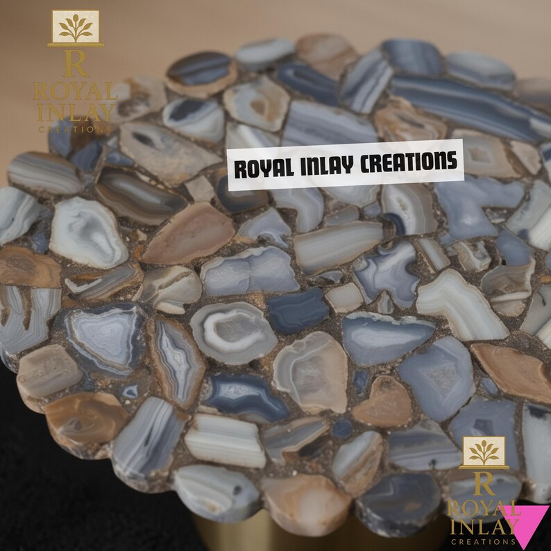 Puede incluir: Una mesa de mosaico con un patr&oacute;n de piedras azules, grises y marrones. El texto "ROYAL INLAY CREATIONS" se muestra en una etiqueta blanca. La mesa es probablemente parte de un mueble decorativo.