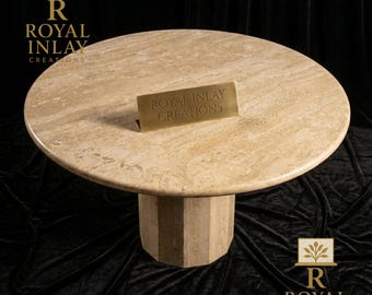 May include: A round, beige marble table with a geometric pedestal base. The table features the text "ROYAL INLAY CREATIONS" on a small brass sign. The table is set against a black background, with the Royal Inlay logo in the corners.