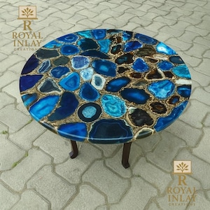 Könnte beinhalten: Ein runder Tisch mit einer Mosaikplatte aus blauen und braunen Achatsteinen. Der Tisch hat dunkelbraune Beine. Der Text "ROYAL INLAY CREATION" ist auf der Seite zu sehen.