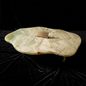 May include: A large, irregularly shaped, green and white onyx table with a polished surface. The table has a small, rectangular brass plaque that reads "ROYAL INLAY CREATIONS". The table is supported by a single, curved leg.