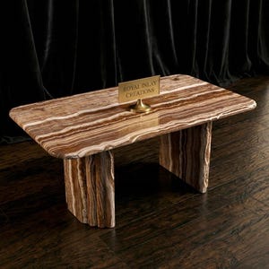 Puede incluir: Una mesa de centro rectangular con un patrón a rayas marrón y crema. La mesa tiene dos patas gruesas y rectangulares. Un pequeño letrero dorado que dice "ROYAL INLAY CREATIONS" está sobre la mesa.