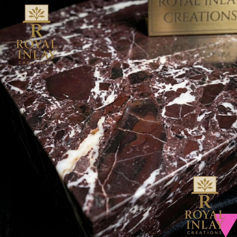 Puede incluir: Primer plano de una secci&oacute;n de una superficie de m&aacute;rmol con un rico color burdeos y vetas blancas. El m&aacute;rmol tiene un acabado pulido y es de Royal Inlay Creations. El logotipo es visible en las esquinas.
