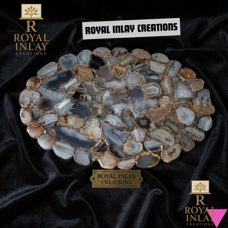 Puede incluir: Bandeja decorativa ovalada hecha de piedras de &aacute;gata incrustadas en tonos grises, azules y marrones. La bandeja presenta un patr&oacute;n similar a un mosaico y est&aacute; colocada sobre un fondo oscuro. Se muestra el texto "ROYAL INLAY CREATIONS".