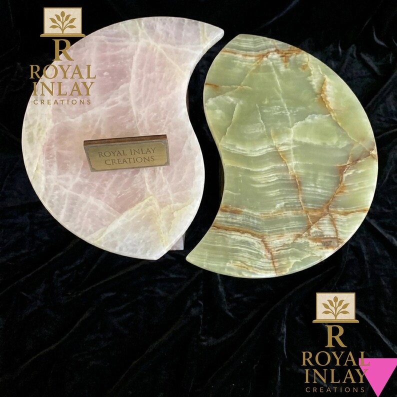 May include: Two decorative onyx pieces, one pink and one green, in a yin-yang design. The pink piece has a light, translucent appearance, while the green piece features brown veining. Each piece has a small, rectangular plaque with the text "ROYAL INLAY CREATIONS".
