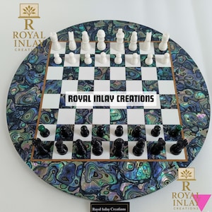 May include: A circular chess set with a mother-of-pearl inlaid border. The chessboard has a white and black chequered pattern. The chess pieces are black and white. The text "ROYAL INLAY CREATIONS" is displayed on the board.