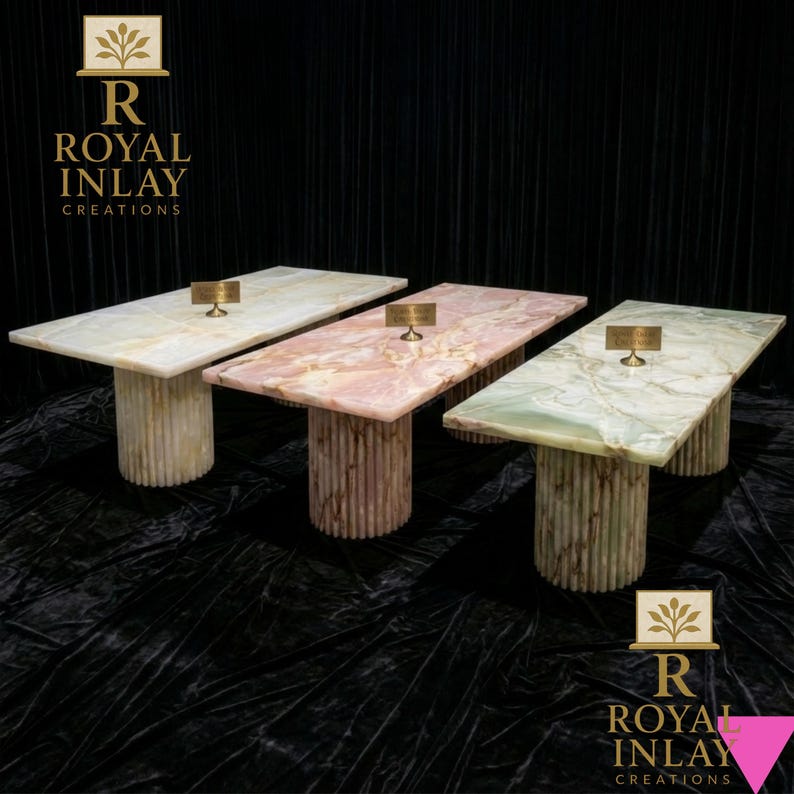 May include: Three rectangular tables with marble tops in cream, pink, and green hues. Each table has a cylindrical base with vertical grooves. The tables are displayed against a black backdrop. The logo "ROYAL INLAY CREATIONS" is visible.