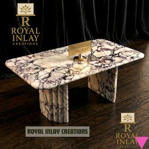 May include: A rectangular marble coffee table with a white and purple veined pattern. The table has a curved edge and two vertical supports. The text "ROYAL INLAY CREATIONS" is displayed on the table and in the logo.