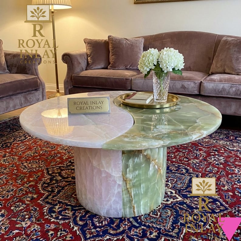 May include: A two-toned coffee table with a pink and green onyx top. The table has a cylindrical base and a yin-yang design. The text "ROYAL INLAY CREATIONS" is visible on the table. A vase of white flowers sits on the table.