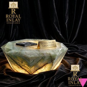 May include: A striking, geometric coffee table with internal lighting. The table is crafted from a translucent, pale green material with a marbled effect. A small book and a gold sign reading "ROYAL INLAY CREATIONS" are on the table.