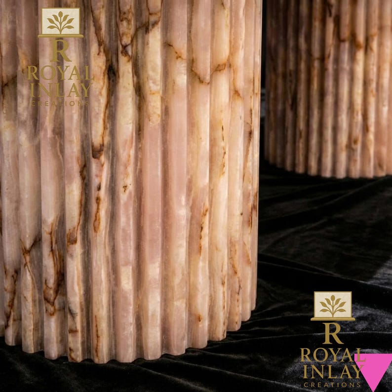 May include: Two cylindrical, fluted columns with a pink and brown marble-like appearance. The columns have vertical grooves and a polished finish. The columns are set against a dark background. The logo "ROYAL INLAY CREATIONS" is visible.