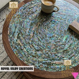 Könnte beinhalten: Runder Couchtisch aus Holz mit einer Mosaikoberfläche aus schillernden Muschelteilen in einem geometrischen Muster. Der Tisch hat einen dunklen Holzrahmen und eine Tasse Kaffee. Der Text "ROYAL INLAY CREATIONS" ist sichtbar.