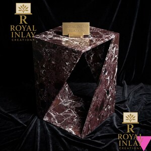 Puede incluir: Una mesa auxiliar geom&eacute;trica de m&aacute;rmol burdeos y blanco veteado. La mesa tiene un dise&ntilde;o angular &uacute;nico con espacios abiertos. Un peque&ntilde;o letrero dorado en la parte superior dice "ROYAL INLAY CREATIONS".