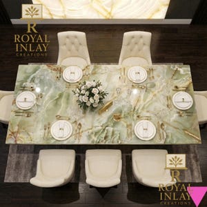 May include: Overhead view of a dining table with a green marble top, set for a meal. The table is surrounded by cream-colored chairs. Gold-colored cutlery and white plates are arranged on the table, along with a floral centerpiece.