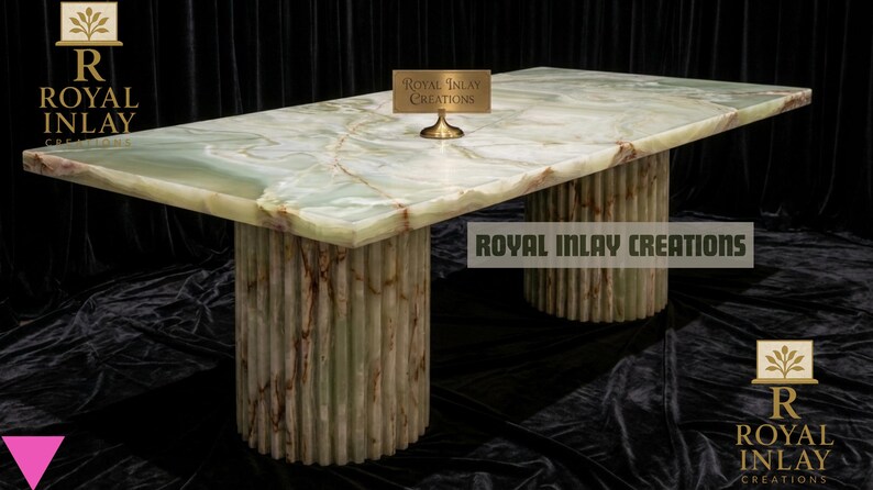May include: A rectangular onyx table with a green and brown marbled surface. The table rests on two cylindrical bases with vertical ribbed detailing. The text "Royal Inlay Creations" is visible on the table and in the logo.