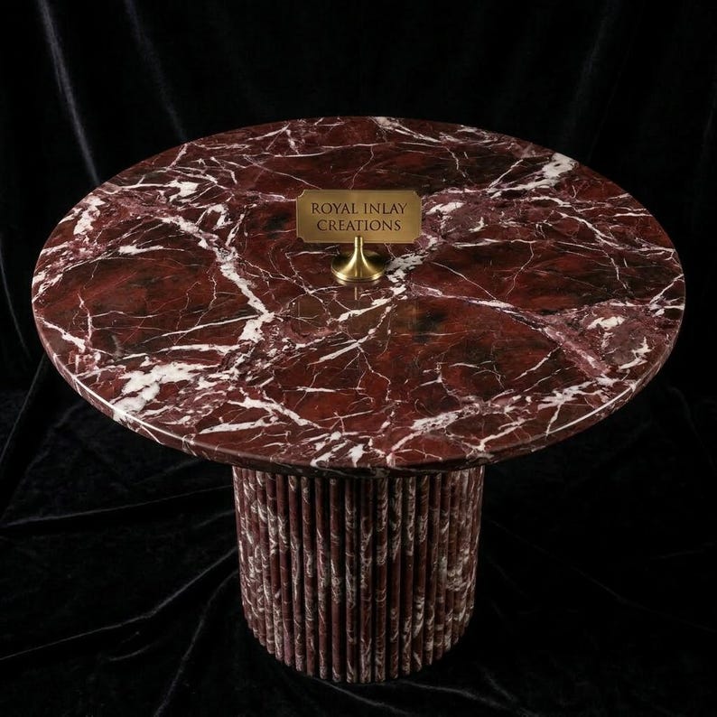 Puede incluir: Una mesa redonda de m&aacute;rmol con una tapa veteada en rojo oscuro y blanco. La base es cil&iacute;ndrica, hecha de piezas verticales de m&aacute;rmol rojo y blanco. Un peque&ntilde;o letrero de lat&oacute;n dice "ROYAL INLAY CREATIONS".