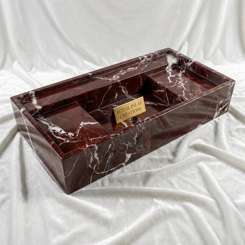 Puede incluir: Una bandeja rectangular de m&aacute;rmol rojo con vetas blancas. La bandeja tiene un compartimento incorporado y una peque&ntilde;a placa dorada que dice "ROYAL INLAY CREATIONS". La bandeja est&aacute; dise&ntilde;ada para uso decorativo o funcional.