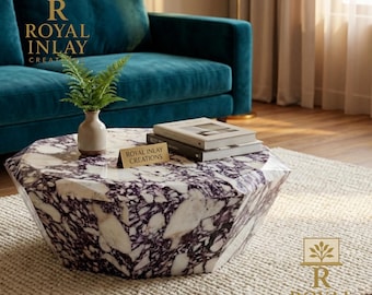 Op de afbeelding: Een zeshoekige salontafel met een wit en paars marmeren blad. De tafel staat voor een turquoise bank en een crèmekleurig tapijt. Een kleine vaas met groen en boeken staan op de tafel. De tafel heeft de tekst "Royal Inlay Creations".