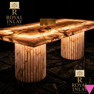 May include: A rectangular table with a glowing, translucent top and two cylindrical, fluted legs. The table's surface has a warm, amber color with brown veining. The table is illuminated from within, creating a soft glow. The table is branded with the text "Royal Inlay Creations".