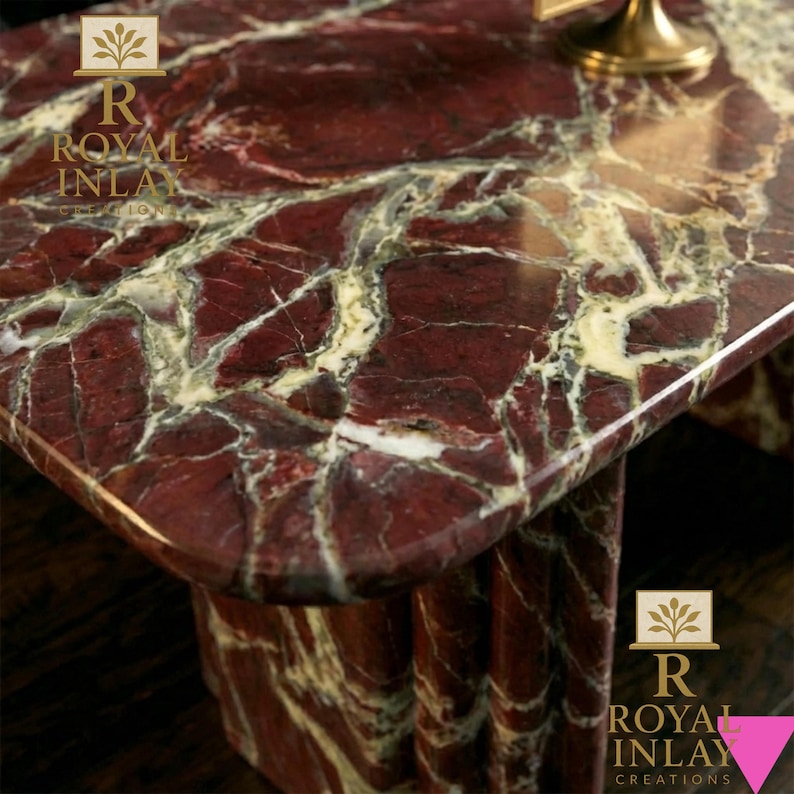 May include: Close-up of a rectangular marble table with a rich red and white veined pattern. The table has rounded corners and a polished surface. The table's base is also made of the same marble.