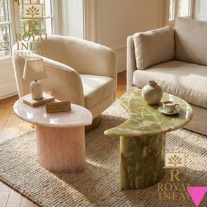 May include: Two unique side tables. One is a light pink, oval-shaped table with a cylindrical base. The other is a green, kidney-shaped table with a cylindrical base. Both tables are made of stone and are in a living room setting.