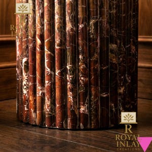 May include: Close-up of a decorative, fluted column made of reddish-brown marble with white veining. The column is set on a dark wood floor. The logo "Royal Inlay Creations" is visible.