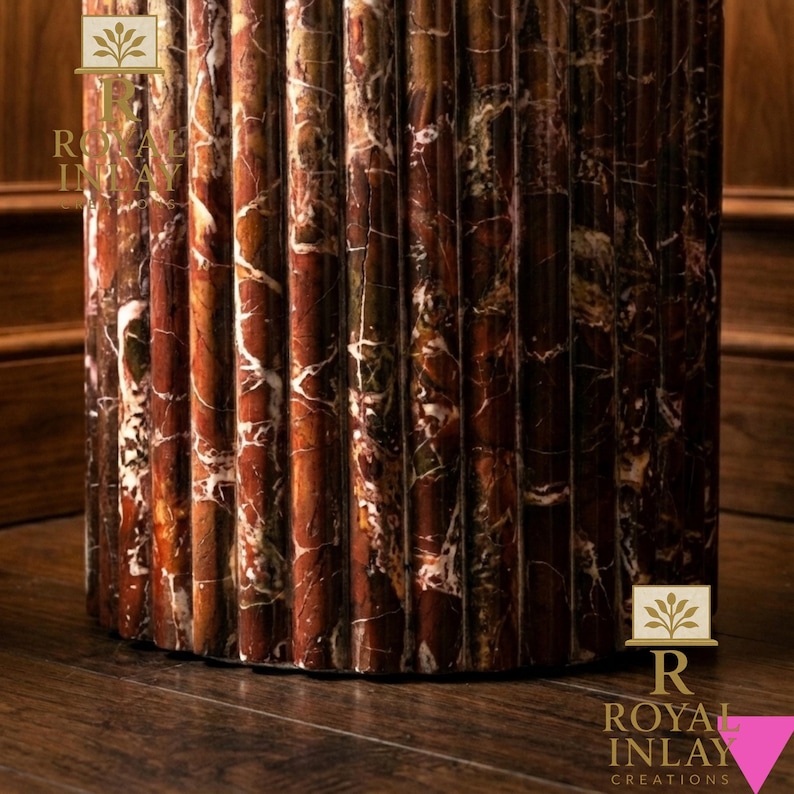 May include: Close-up of a decorative, fluted column made of reddish-brown marble with white veining. The column is set on a dark wood floor. The logo "Royal Inlay Creations" is visible.