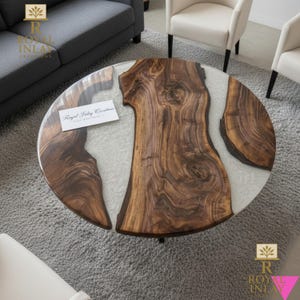 May include: Round coffee table with a unique design. The table features a clear resin top with sections of natural wood grain and a light gray infill. The table is supported by black metal legs. A business card with text is on the table.