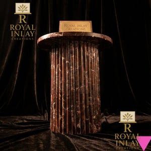 May include: A decorative, cylindrical pedestal with a fluted design. The pedestal is made of a reddish-brown marble with white veining. The top of the pedestal has a circular shape. The text "Royal Inlay Creations" is displayed on a small plaque on top.