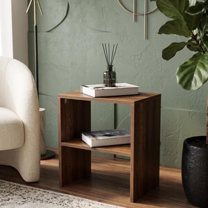 Könnte beinhalten: Ein rechteckiger Beistelltisch aus Holz mit dunkelbrauner Holzmaserung, der ein offenes Design mit einem mittleren Regalboden aufweist. Auf der Tischplatte stehen ein weißes Buch und ein Glas-Diffusor, auf dem unteren Boden liegt ein weiteres Buch.