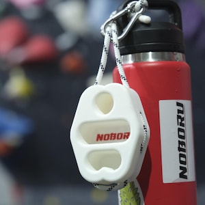 May include: White plastic climbing hold with the word "NOBORU" printed in red. The hold is attached to a red water bottle with a black lid and a white sticker with the word "NOBORU" printed in black.