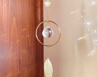 May include: A gold-toned crystal suncatcher with a clear crystal ball hanging from a gold ring. The suncatcher also has a gold leaf charm hanging from the bottom.