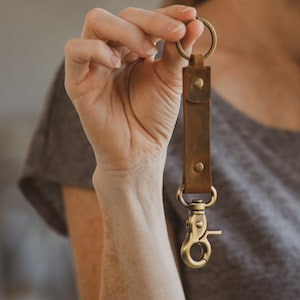Puede incluir: Un llavero de cuero marrón con un anillo de llaves de latón y un clip de latón.