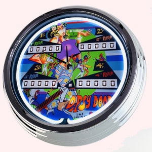 Può includere: Un orologio rotondo con cornice argentata e un design di flipper retrò colorato. Il quadrante dell'orologio presenta uno sfondo blu con un design di flipper verde, giallo e viola. Il quadrante dell'orologio include anche il testo "Dizzy Doo" e "1 to 4 can play".