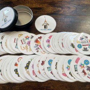 May include: A set of 36 round white cards with colorful illustrations and text. The cards are in a metal tin with the text "EDUC'LAND E" and a website address.