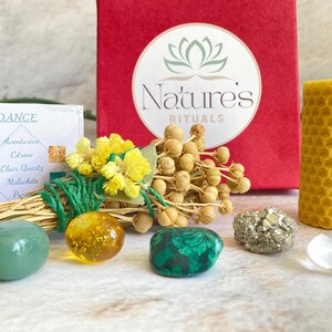 May include: A green and gold abundance ritual kit with a small box, a candle, crystals, and dried flowers. The box says "Nature's Rituals" and the card says "Abundance".