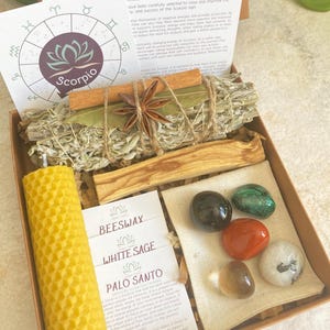 May include: A wooden box filled with crystals, a beeswax candle, white sage, palo santo, and a small bag of herbs. The box is decorated with a zodiac symbol for Scorpio and the text "STALS FOR SCORPIO".
