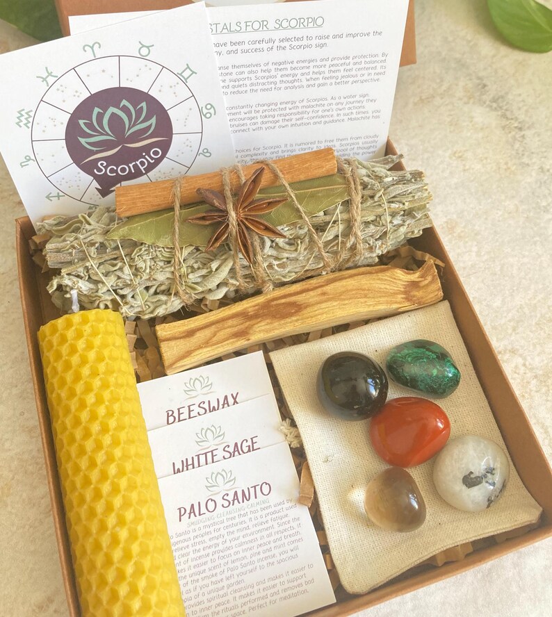May include: A wooden box filled with crystals, a beeswax candle, white sage, palo santo, and a small bag of herbs. The box is decorated with a zodiac symbol for Scorpio and the text "STALS FOR SCORPIO".