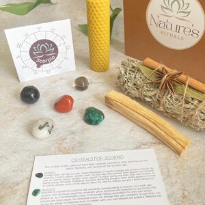 May include: A set of crystals for Scorpio zodiac sign, including obsidian, malachite, and moonstone. The set also includes a yellow beeswax candle, a bundle of sage, and a palo santo stick. The crystals are arranged on a white surface with a card that reads "Crystals for Scorpio".