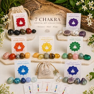 May include: A collection of seven chakra crystal sets, each with a corresponding card and gemstones. The cards are labeled with chakra names and feature a lotus flower design. The crystals are in various colors and shapes.