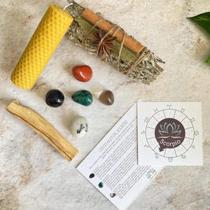 May include: A set of crystals for Scorpio zodiac sign, including a black obsidian, green aventurine, clear quartz, red carnelian, and a white crystal. The set also includes a sage smudge stick, a palo santo stick, and a honeycomb candle. The card includes the text "Crystals for Scorpio" and a zodiac wheel with the Scorpio sign.
