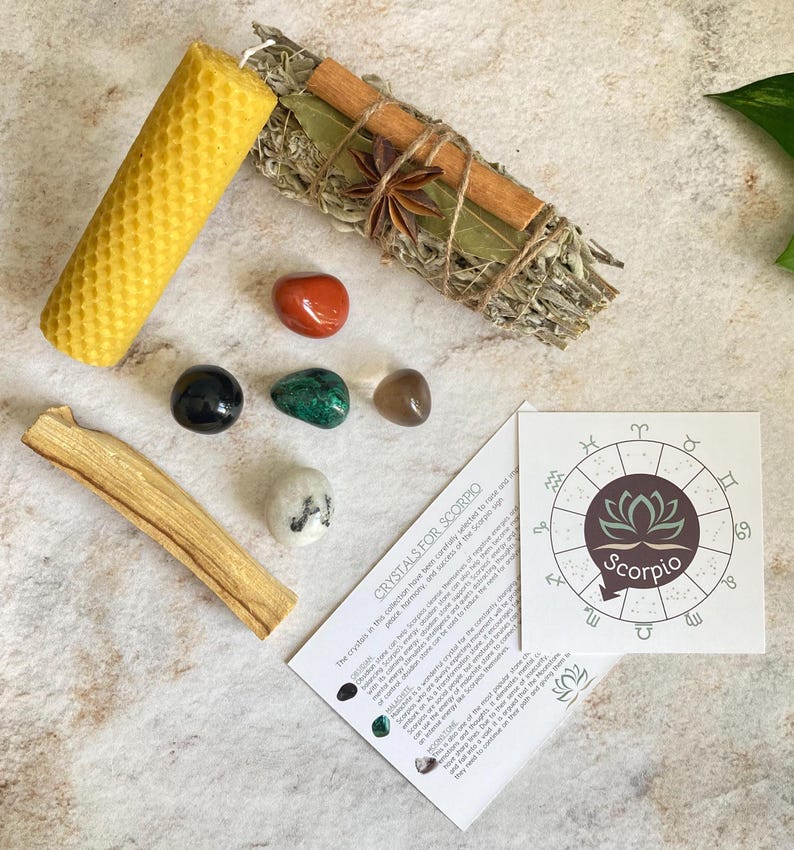 May include: A set of crystals for Scorpio zodiac sign, including a black obsidian, green aventurine, clear quartz, red carnelian, and a white crystal. The set also includes a sage smudge stick, a palo santo stick, and a honeycomb candle. The card includes the text "Crystals for Scorpio" and a zodiac wheel with the Scorpio sign.